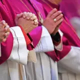 Geistliche in violetten Roben beten. Auch ein Pfarrer zahlt Kirchensteuer, wie die Ringe an den Fingern zeigen.