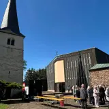 Menschen versammeln sich vor einer Kirche mit einem alten Turm. Die Frage "was ist Profanierung" könnte hier aufkommen, wenn die Kirche nicht mehr als Gotteshaus genutzt wird.