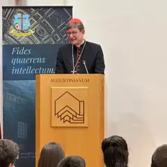 Kardinal Woelki spricht vor Zuhörern im Augustinianum. Er trägt eine schwarze Soutane und einen roten Pileolus.