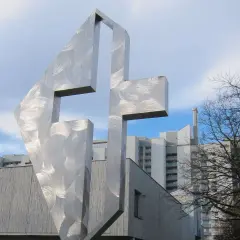 Modernes Kreuz aus gebürstetem Metall vor der Kirche St. Lukas Westkreuz.