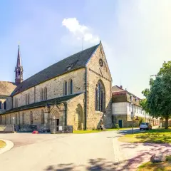 Klosterkirche mit Turm, Teil des Jakobsweg Hessen. Ein Paar sitzt auf einer Bank im Schatten eines Baumes.