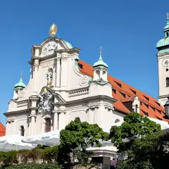 Prachtvolle Kirche am Viktualienmarkt mit goldenem Stern und Glockenturm. Sonnige Szene mit Cafés und Grünflächen.