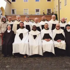 Gruppe von unbeschuhten Karmeliten in braunen Kutten und weißen Umhängen posiert vor einem gelben Gebäude.