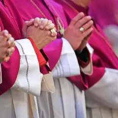 Geistliche in violetten Roben beten. Auch ein Pfarrer zahlt Kirchensteuer, wie die Ringe an den Fingern zeigen.