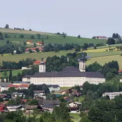 Das Stift Schlierbach, ein imposantes Barockgebäude, thront über einer malerischen Landschaft mit grünen Hügeln und traditionellen Häusern.