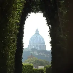 Blick durch einen grünen Torbogen auf die Kuppel des Petersdoms in Rom. Ein Ort, der an den Malteser Orden Rom erinnert.