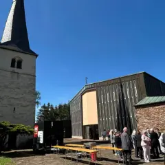 Menschen versammeln sich vor einer Kirche mit einem alten Turm. Die Frage "was ist Profanierung" könnte hier aufkommen, wenn die Kirche nicht mehr als Gotteshaus genutzt wird.