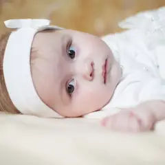 Ein süßes Baby in weißer Taufkleidung, mit einem Stirnband und einer Schleife. Vielleicht ein Name wie Maria oder Anna, typisch für katholische heilige Namen weiblich.