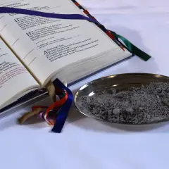 Ein aufgeschlagenes Buch mit Gebeten und eine Schale mit Asche. "Aus Staub bist du zu Staub wirst du" – ein Symbol für Vergänglichkeit.