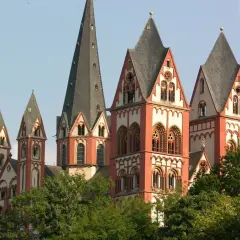 Der Limburger Dom mit seinen roten Türmen ragt über grünen Bäumen auf. Man munkelt, der Bischof von Limburg hätte dort eine goldene Badewanne versteckt.