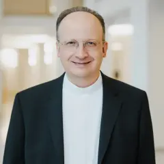 Ein Mann mit Brille trägt ein schwarzes Sakko über einem weißen Hemdkragen. Er lächelt freundlich. Er könnte ein Generalvikar sein, der die Stellvertretung des Bischofs übernimmt.