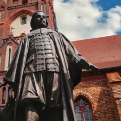 Bronzestatue von Paul Gerhardt vor einer roten Backsteinkirche mit blauen Himmel und Wolken.