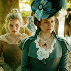 Zwei Frauen in historischer Kleidung, eine mit auffälligem Hut, im Wald. Was bedeutet Gloria? Vielleicht die Pracht ihrer Gewänder.