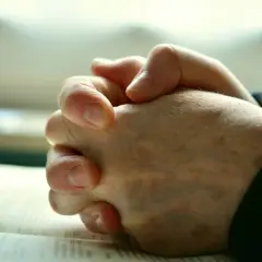 Gefaltete Hände über einem Buch, ein Zeichen von Glauben und dem Ringen mit **Gott und dem Leid**.