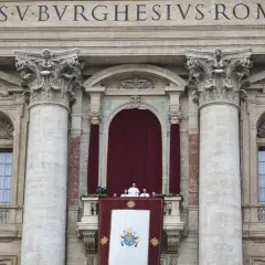 Der Papst steht auf dem Balkon des Petersdoms, umgeben von Kardinälen. Ein großes Wappen hängt über dem Balkon.