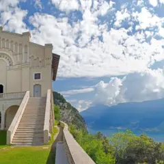 Kirche auf einem Hügel mit Blick auf einen See und Berge unter blauem Himmel mit Wolken.
