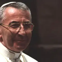 Porträt von Papst Johannes Paul I. mit Brille, im Hintergrund eine goldene Statue.