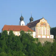 Prachtvolles Kloster Baumburg thront auf einem Hügel, umgeben von üppigem Grün. Zwei markante Zwiebeltürme ragen in den blauen Himmel.