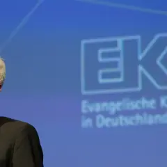 Lächeln des EKD Vorsitzenden vor dem Logo der Evangelischen Kirche in Deutschland.