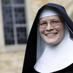 Lächelnde Nonne mit Brille vor einem Kloster. Sie hat sich entschieden, ins Kloster zu gehen und strahlt Zufriedenheit aus.