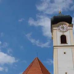 Der Turm der Stadtkirche Bad Aibling ragt in den blauen Himmel mit weißen Wolken.