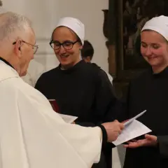 Priester übergibt Dokumente an zwei Dienerinnen vom Heiligen Blut, die lächelnd ihre Aufgaben annehmen.