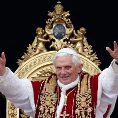 Papst Benedikt XVI. winkt in prächtiger Papst-Kleidung, mit weißer Soutane und rotem Umhang, verziert mit goldenen Stickereien.