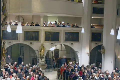 Menschen in der Stadtkirche Wolfratshausen, einige auf der Empore, andere im Kirchenschiff.