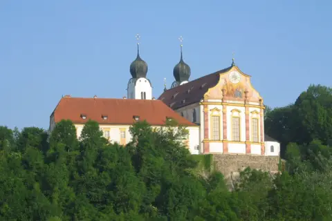 Prachtvolles Kloster Baumburg thront auf einem Hügel, umgeben von üppigem Grün. Zwei markante Zwiebeltürme ragen in den blauen Himmel.