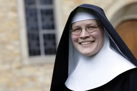 Lächelnde Nonne mit Brille vor einem Kloster. Sie hat sich entschieden, ins Kloster zu gehen und strahlt Zufriedenheit aus.