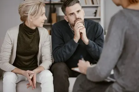 Ein Paar sitzt auf einer Couch und spricht mit einer Person, die Notizen macht. Sie sind in einer Sitzung zur Eheberatung.
