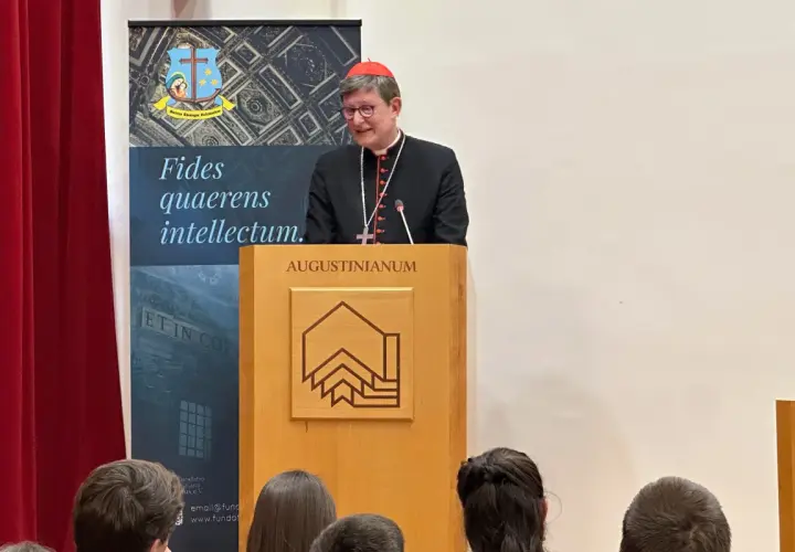 Kardinal Woelki spricht vor Zuhörern im Augustinianum. Er trägt eine schwarze Soutane und einen roten Pileolus.