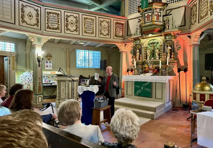 Ein Mann spricht in einer Kirche vor Zuhörern. Er hält ein Buch hoch, das von seelischem Widerstand handeln könnte.
