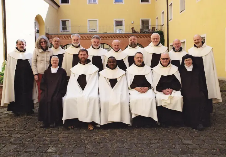 Gruppe von unbeschuhten Karmeliten in braunen Kutten und weißen Umhängen posiert vor einem gelben Gebäude.