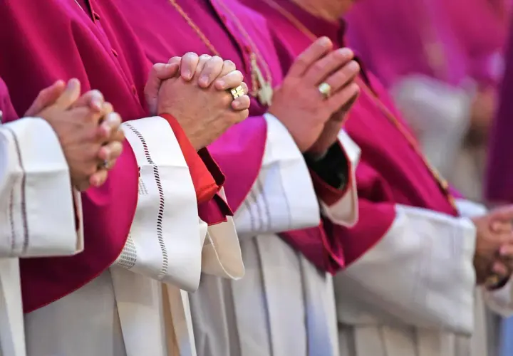 Geistliche in violetten Roben beten. Auch ein Pfarrer zahlt Kirchensteuer, wie die Ringe an den Fingern zeigen.