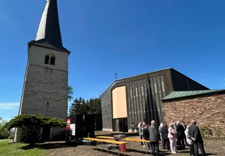 Menschen versammeln sich vor einer Kirche mit einem alten Turm. Die Frage "was ist Profanierung" könnte hier aufkommen, wenn die Kirche nicht mehr als Gotteshaus genutzt wird.