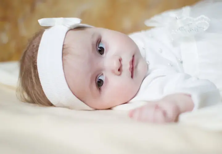 Ein süßes Baby in weißer Taufkleidung, mit einem Stirnband und einer Schleife. Vielleicht ein Name wie Maria oder Anna, typisch für katholische heilige Namen weiblich.