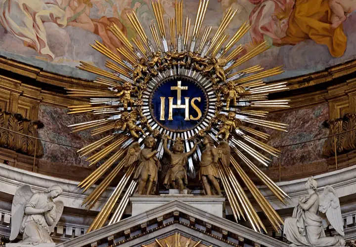 Goldene Strahlenkrone mit IHS-Monogramm, das die Bedeutung von Jesus Christus symbolisiert, umgeben von Engeln und Putten.