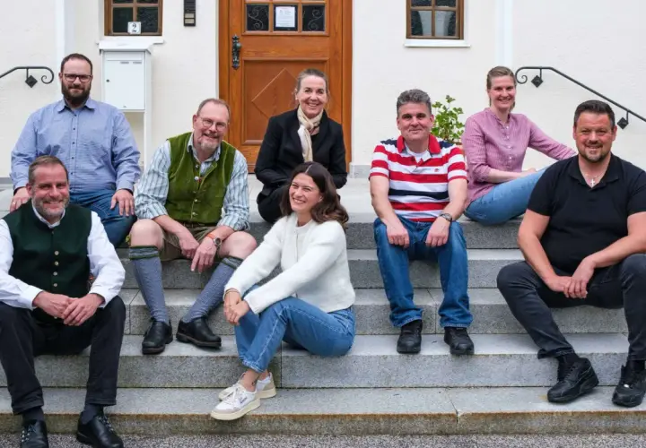 Eine Gruppe von Menschen sitzt lächelnd auf einer Treppe. Sie scheinen Teil einer Gemeinschaft zu sein, vielleicht ein Dekanat, das sich für ein Foto versammelt hat.