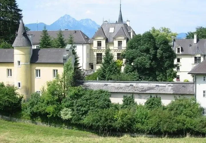 Gelbes Gebäude mit Türmchen und Bergkulisse, erinnert an ein Kloster in Salzburg.