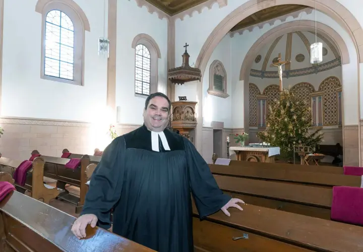 Ein Geistlicher in der Kirche, der die Bänke zeigt. Er wirkt freundlich, als würde er die Bedeutung von Gemeinschaft und Glauben erklären, im Gegensatz zur simonie definition.