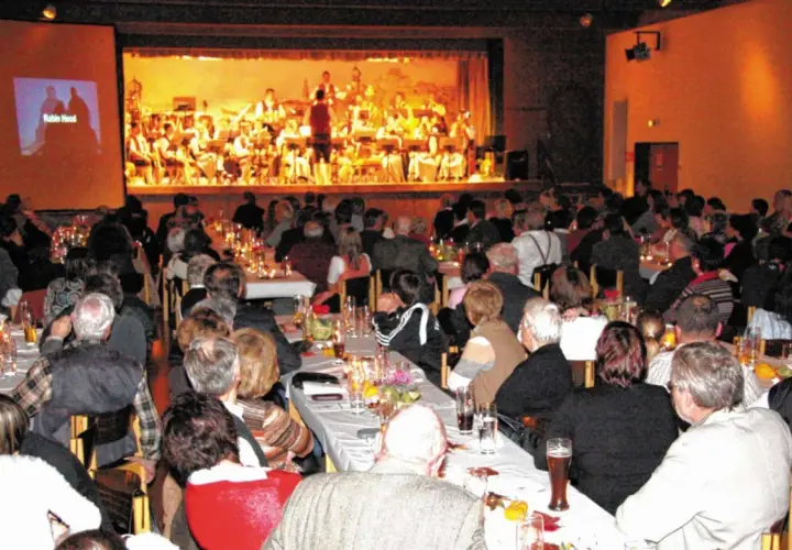 Festliches Bankett im bischof bernhard haus kraiburg. Gäste lauschen einem Orchester, während auf der Leinwand "Robin Hood" läuft.