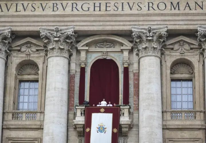 Der Papst steht auf dem Balkon des Petersdoms, umgeben von Kardinälen. Ein großes Wappen hängt über dem Balkon.