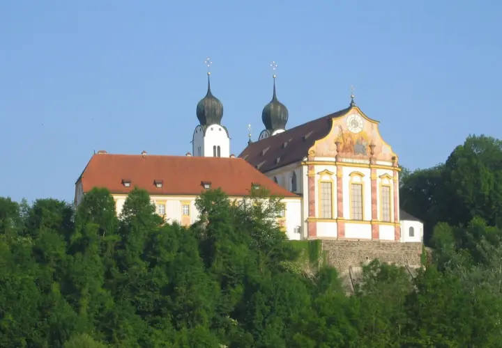 Prachtvolles Kloster Baumburg thront auf einem Hügel, umgeben von üppigem Grün. Zwei markante Zwiebeltürme ragen in den blauen Himmel.
