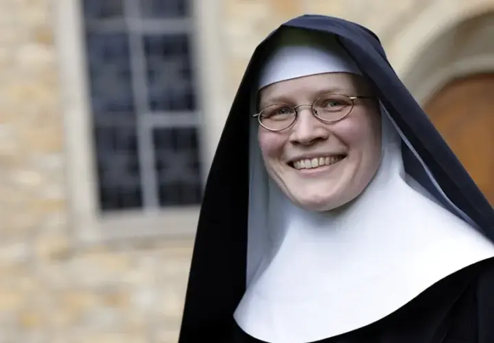 Lächelnde Nonne mit Brille vor einem Kloster. Sie hat sich entschieden, ins Kloster zu gehen und strahlt Zufriedenheit aus.