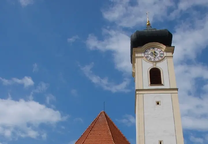 Der Turm der Stadtkirche Bad Aibling ragt in den blauen Himmel mit weißen Wolken.