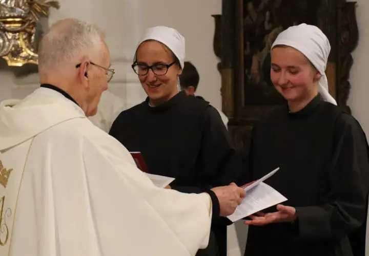 Priester übergibt Dokumente an zwei Dienerinnen vom Heiligen Blut, die lächelnd ihre Aufgaben annehmen.