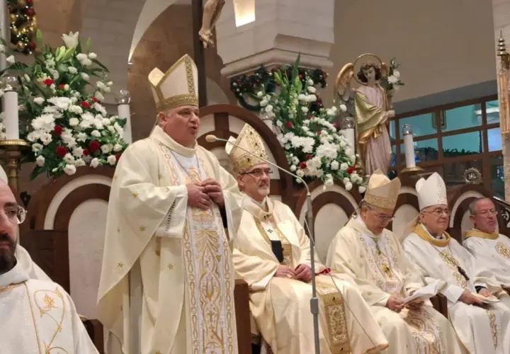 Bischof Konrad Krajewski spricht zu einer Gruppe von Geistlichen in festlicher Kleidung, umgeben von Blumen und religiösen Statuen.
