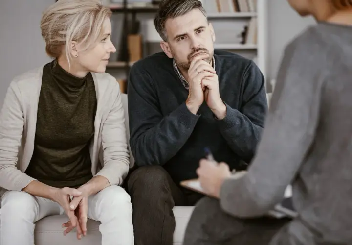 Ein Paar sitzt auf einer Couch und spricht mit einer Person, die Notizen macht. Sie sind in einer Sitzung zur Eheberatung.