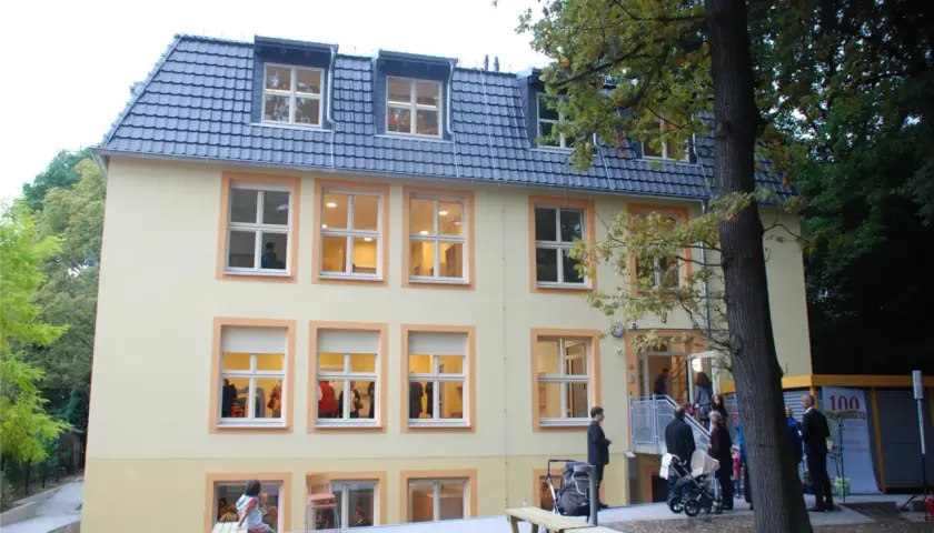 Das Gebäude des Kindergartens St. Klara, ein hellgelbes Haus mit vielen Fenstern, lädt zum Spielen ein.